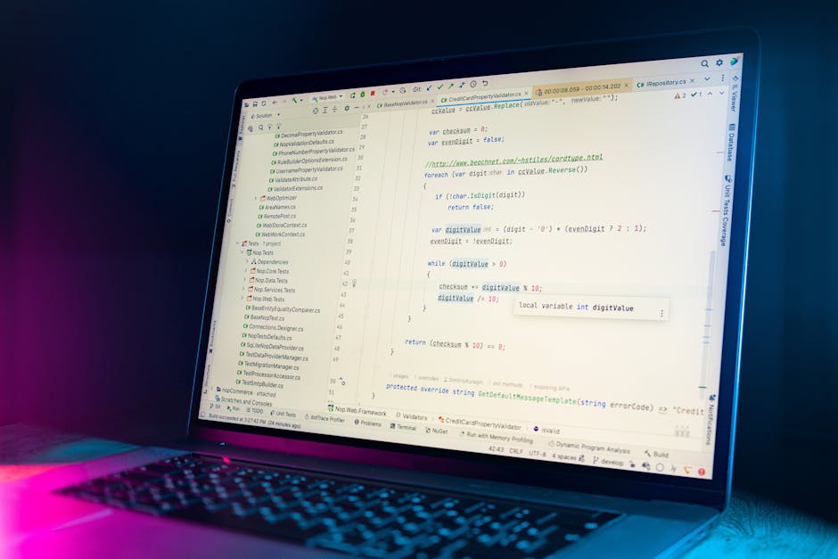 A close-up view of a laptop screen displaying lines of programming code in a text editor, with the code highlighting variable assignments and functions. The laptop has a dark casing with a keyboard il