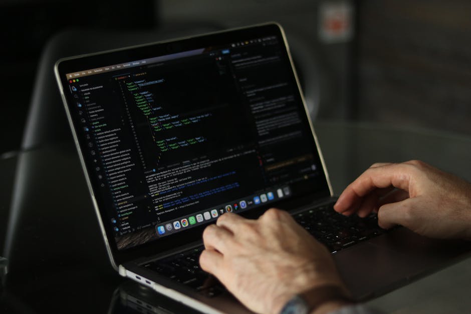 A close-up view of a laptop screen displaying lines of programming code in a text editor, with the code highlighting variable assignments and functions. The laptop has a dark casing with a keyboard il